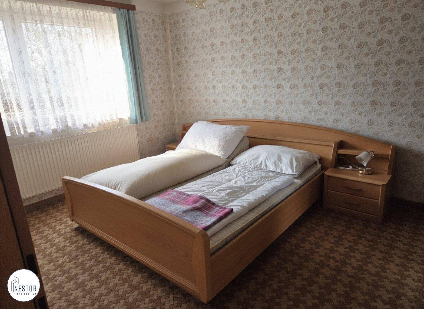 Schlafzimmer mit Doppelbett, Nachttischen und gemusterter Tapete.