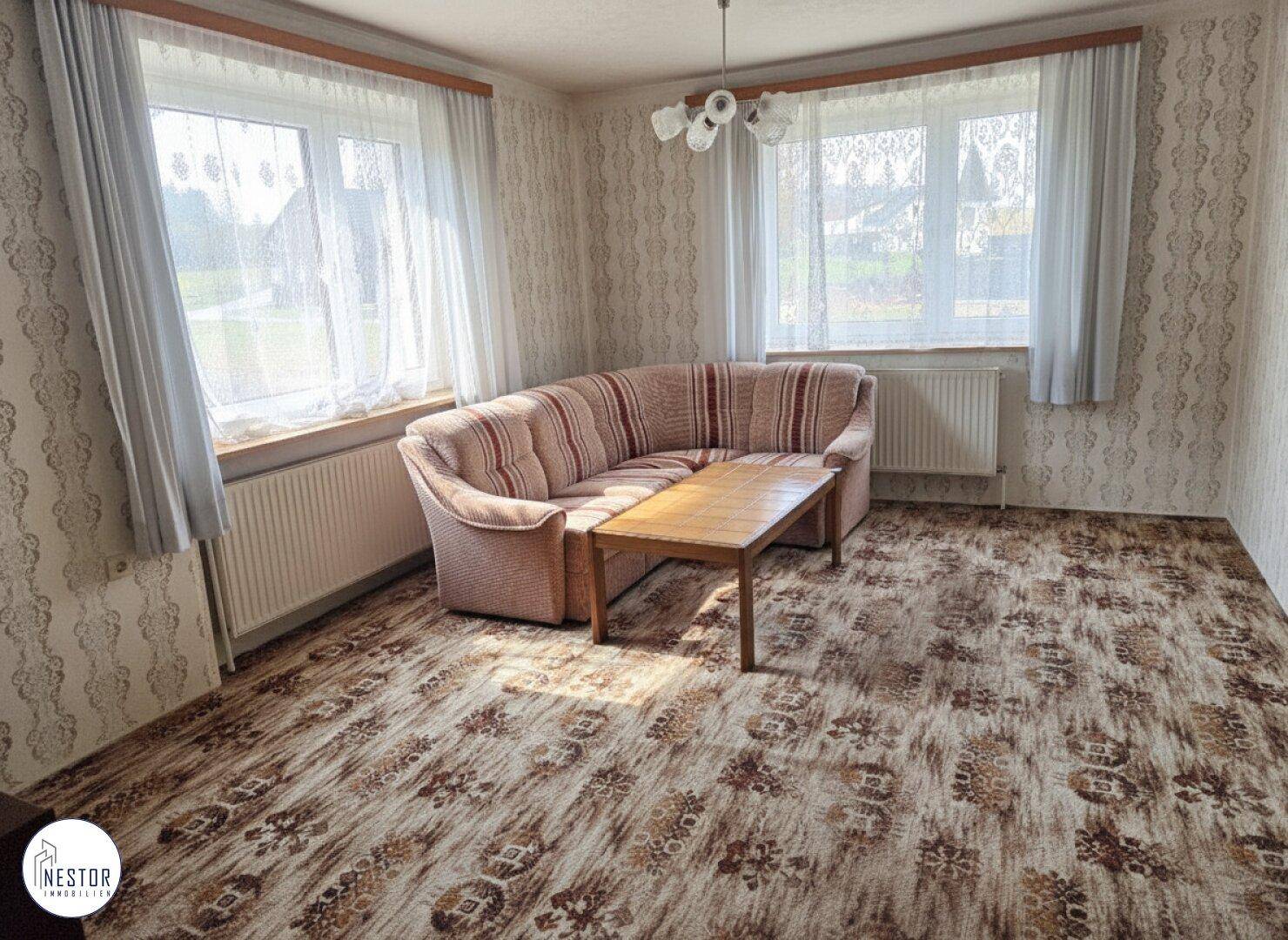 Wohnzimmer mit gemustertem Teppichboden, Sofa und großen Fenstern.