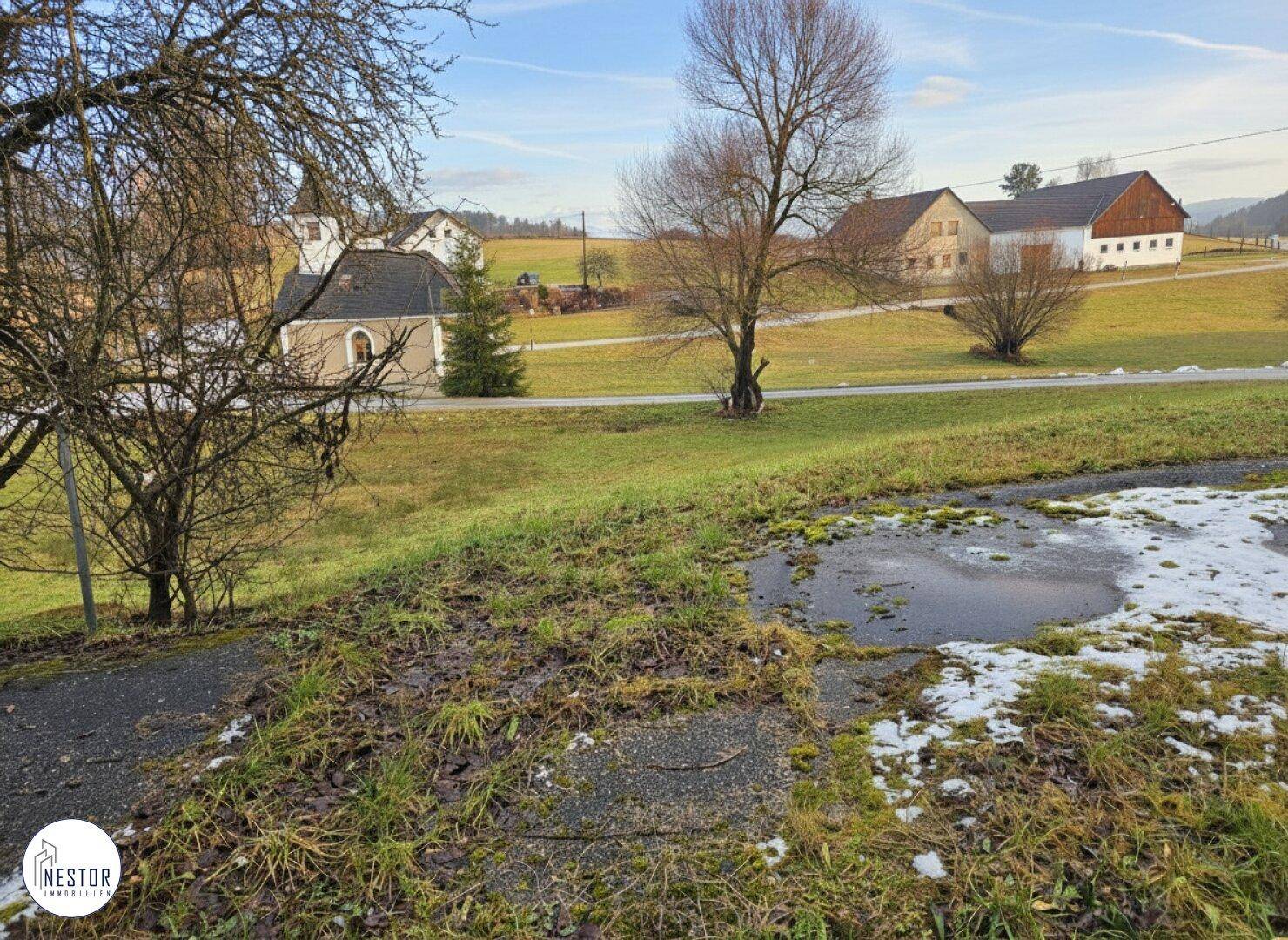 Weitläufige ländliche Umgebung mit Feldern, Bäumen und weiteren Gebäuden in der Ferne.