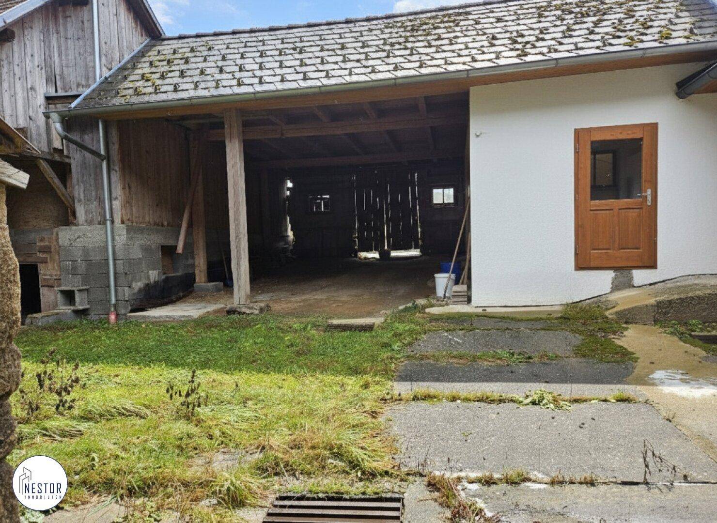 Offener Scheunenbereich mit Holzbalken und Zugang zum Innenhof des Anwesens.
