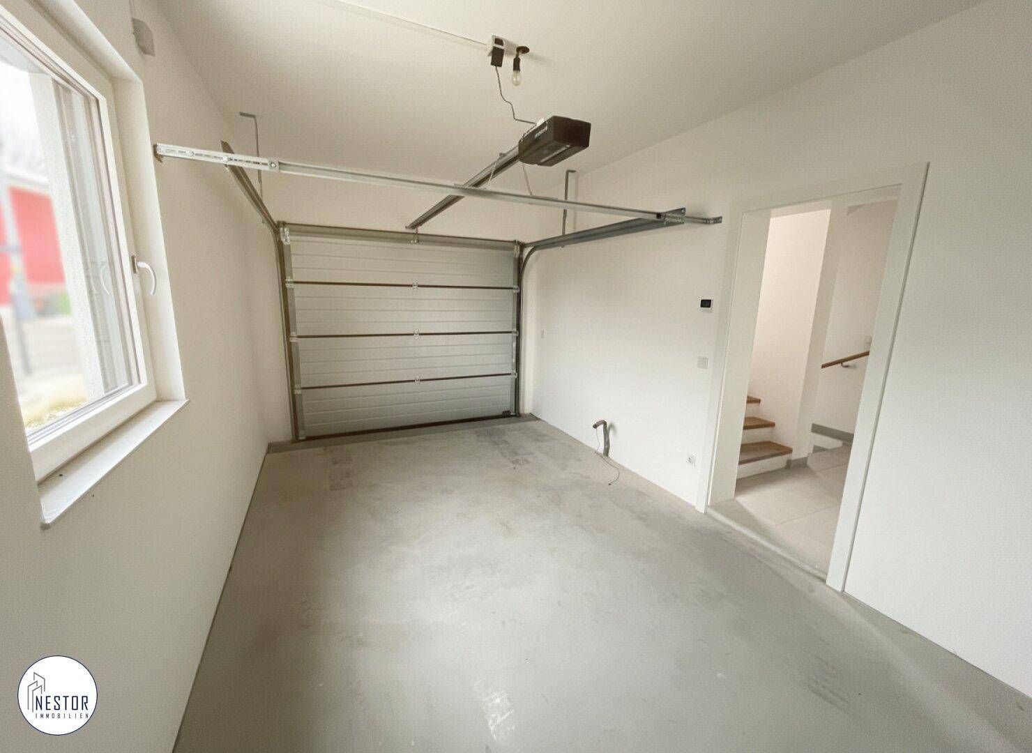 Leere Garage mit Rolltor, Fenster und Zugang zum Treppenhaus.
