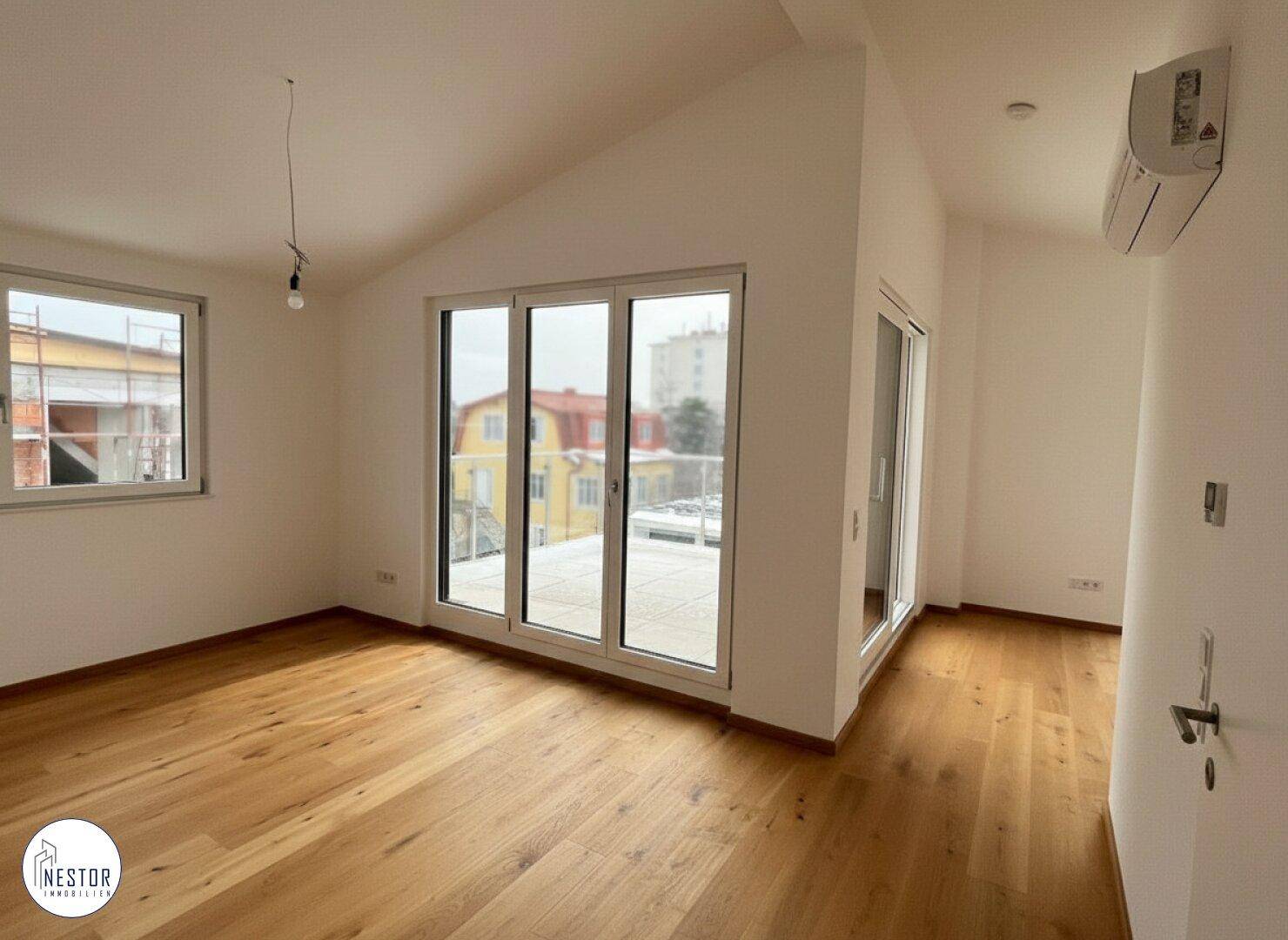 Geräumiger Raum im Dachgeschoss mit Holzboden, Schrägdach und Zugang zur Dachterrasse.