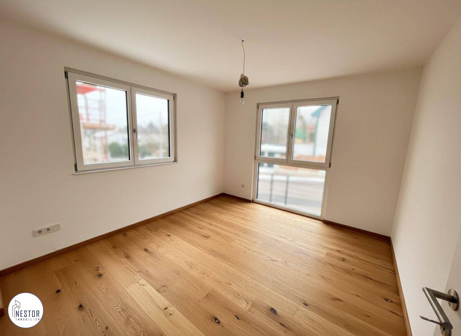 Helles Schlafzimmer mit Holzboden und zwei großen Fenstern.