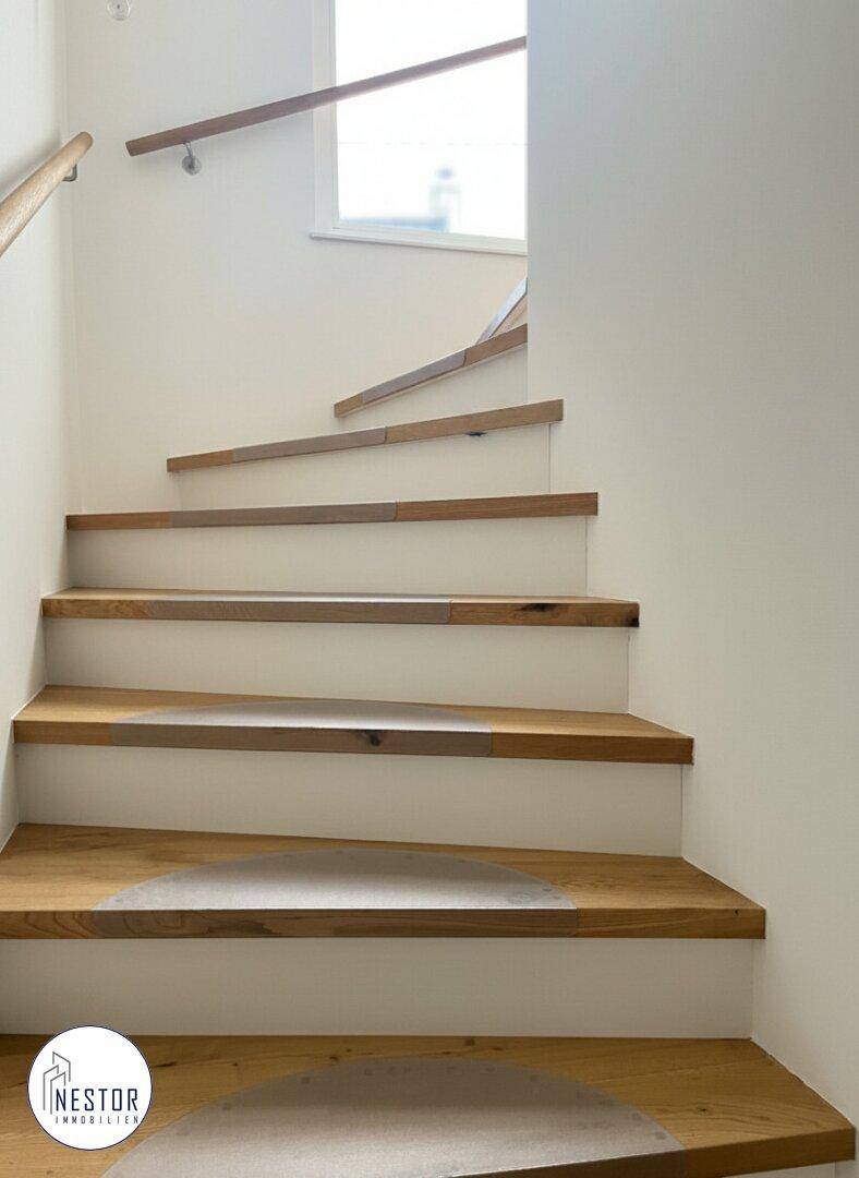 Treppenhaus mit Holzstufen und weiß gestrichenen Wänden.