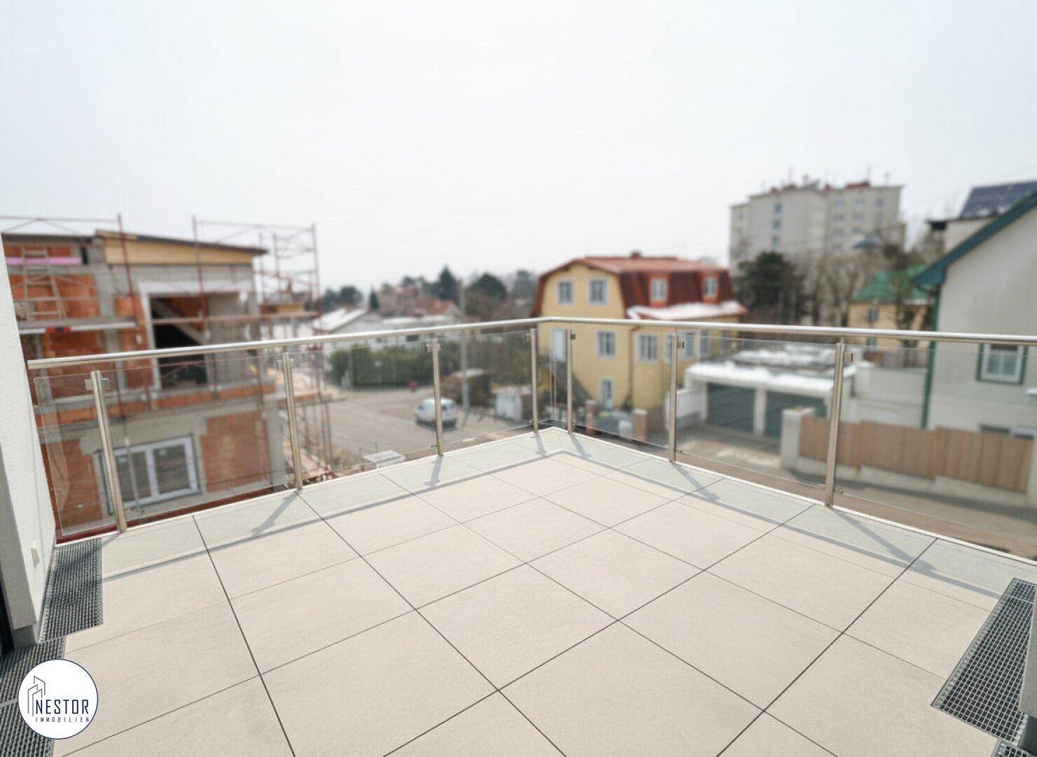 Geräumige Dachterrasse mit Fliesenboden und Glasgeländer, bietet weite Aussicht.