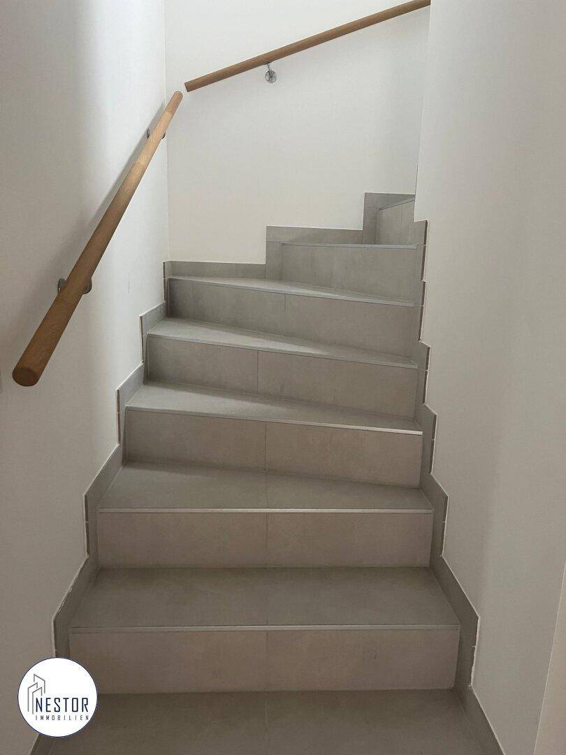 Modernes Treppenhaus mit gefliesten Stufen und Holzhandlauf.