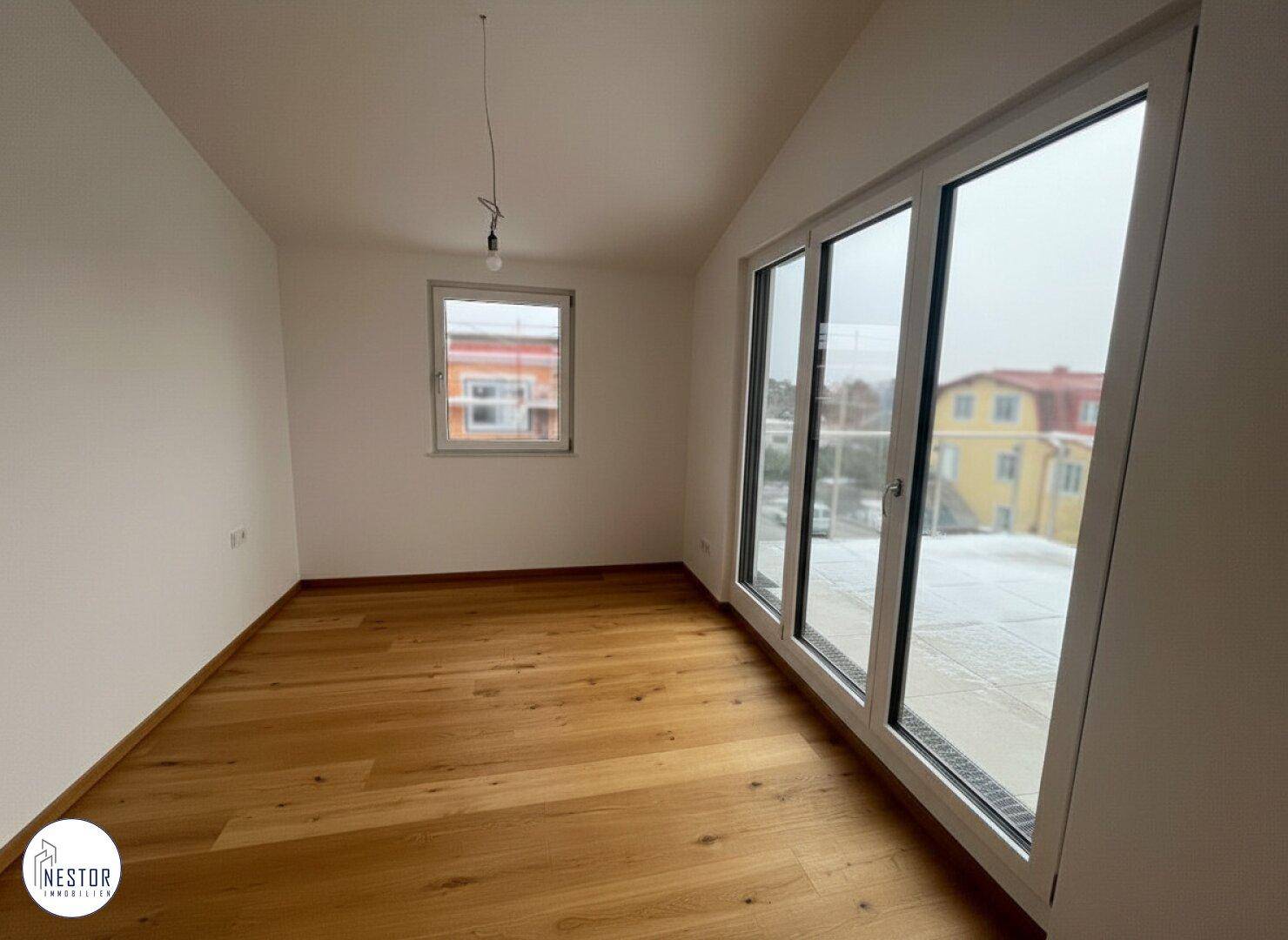Helles Zimmer im Dachgeschoss mit Holzboden, Schrägdach und großen Fenstern.
