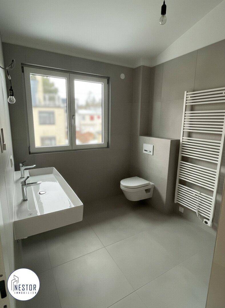 Modernes Badezimmer mit Doppelwaschbecken, wandhängendem WC und beheiztem Handtuchhalter.