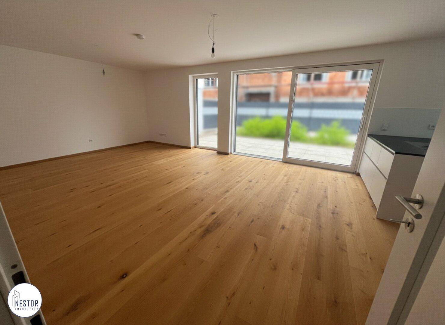Heller offener Wohnbereich mit Holzboden und großen Fenstern zum Außenbereich.