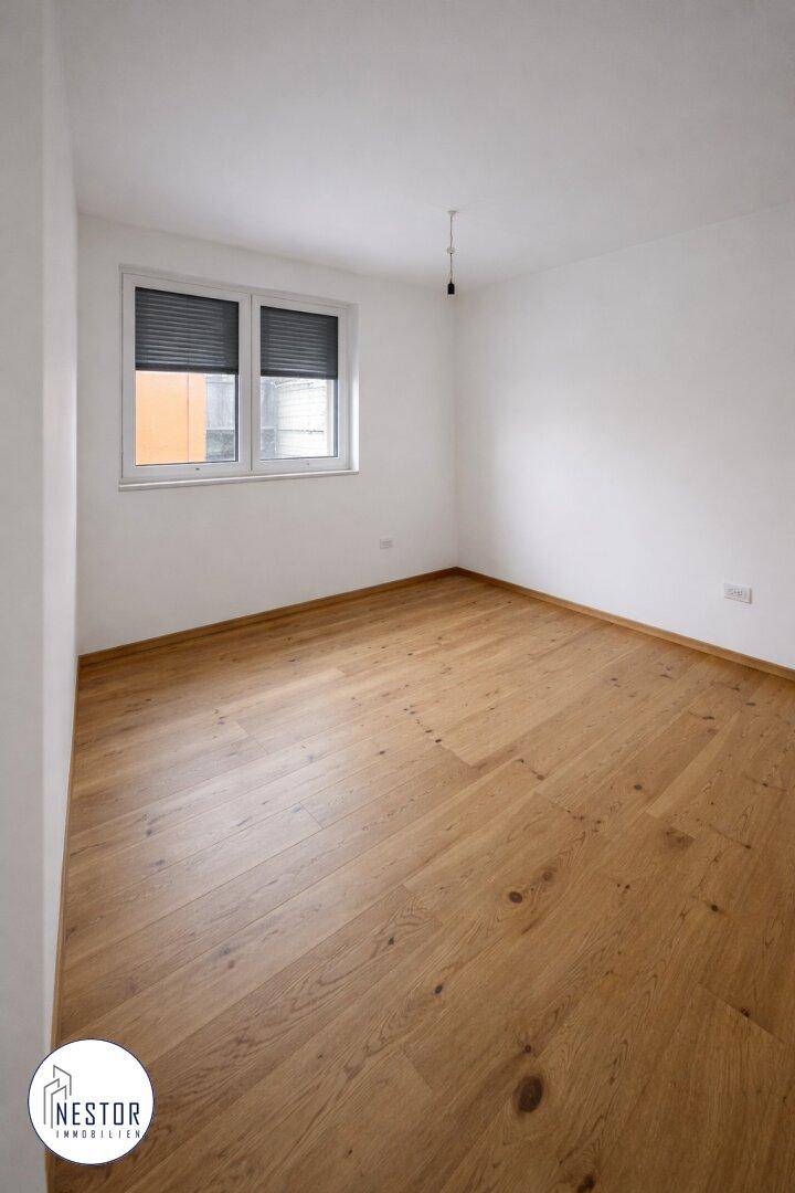 Leeres Zimmer mit Holzboden und einem Fenster mit Rollläden, ideal als Schlaf- oder Arbeitszimmer.