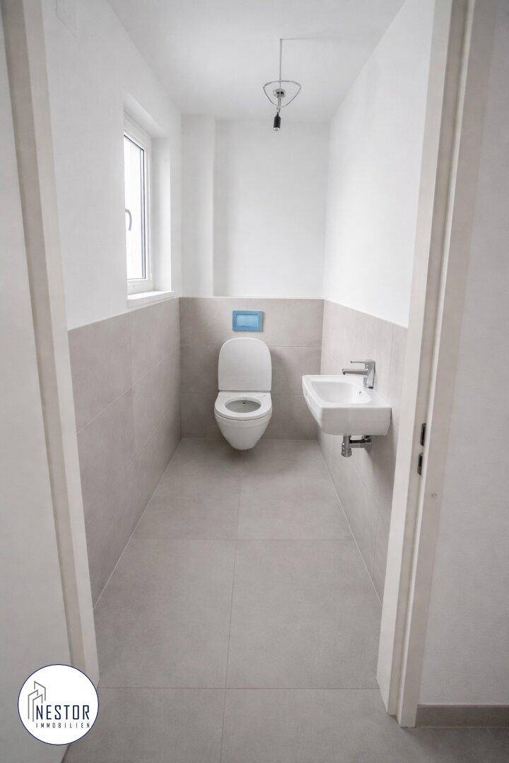 Modernes Gäste-WC mit wandhängendem WC, kleinem Waschbecken und einem Fenster.