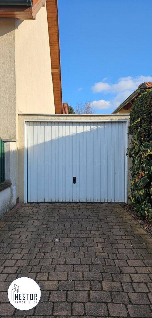 Weißes Garagentor mit gepflasterter Einfahrt unter klarem blauem Himmel.
