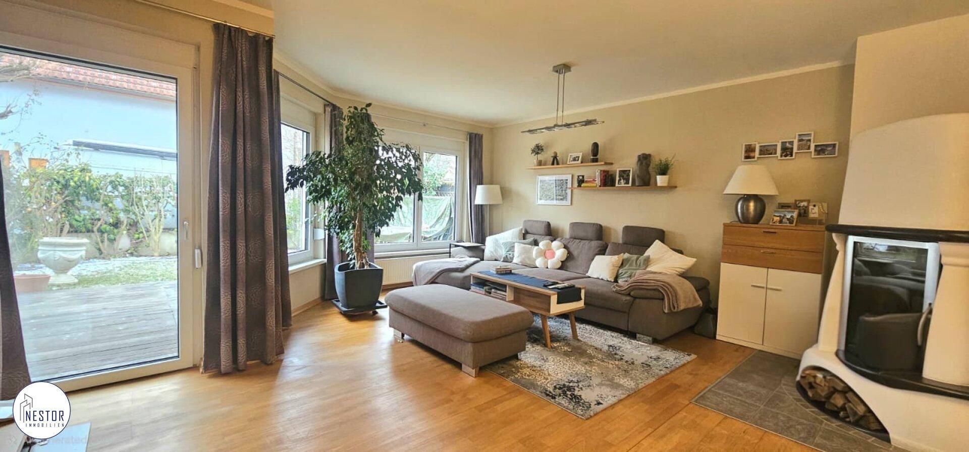 Gemütliches Wohnzimmer mit Kamin, Parkettboden und Blick in den grünen Garten.