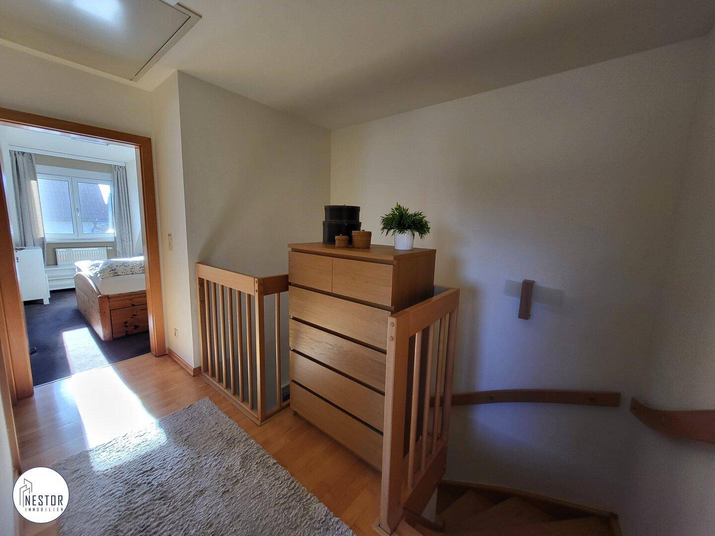 Heller Flur im Obergeschoss mit Holzgeländer und Zugang zu den Zimmern.