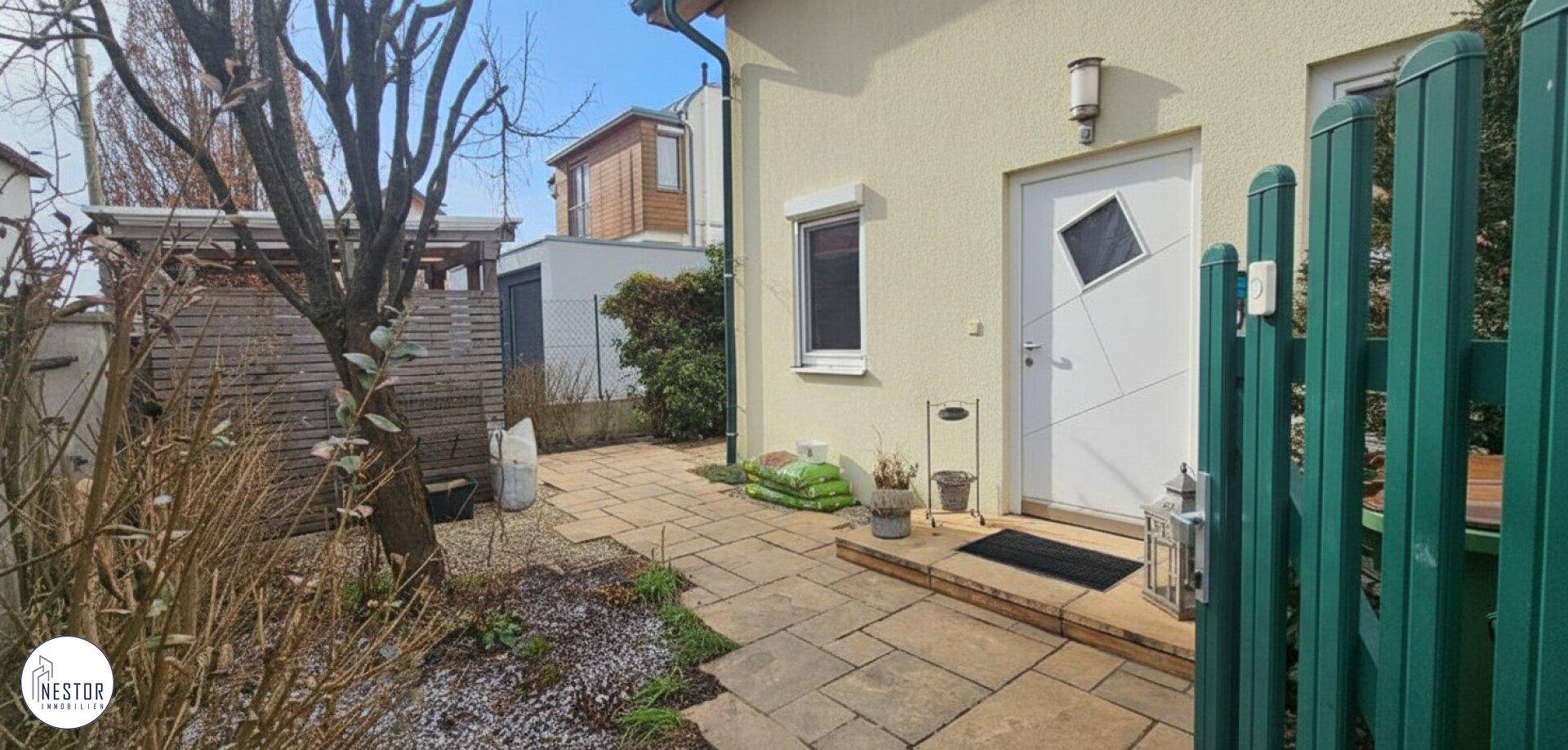 Eingangsbereich des Hauses mit gepflastertem Weg und grüner Pforte.