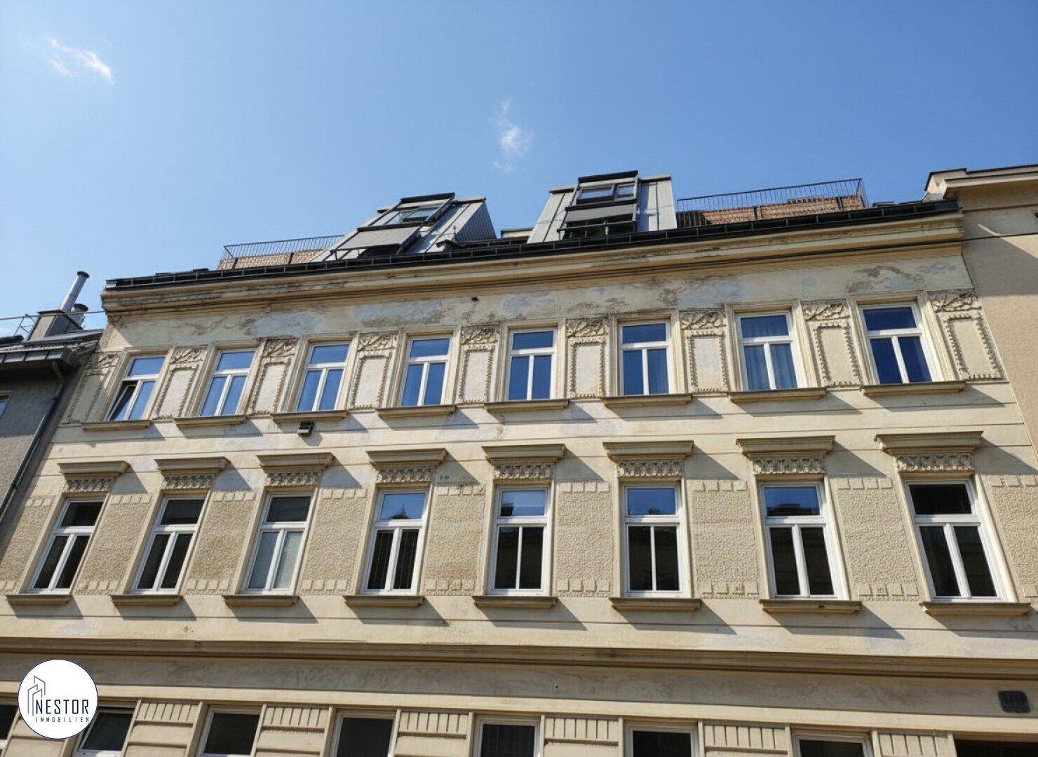 Historische Fassade eines Mehrfamilienhauses mit Dachausbau und vielen Fenstern.
