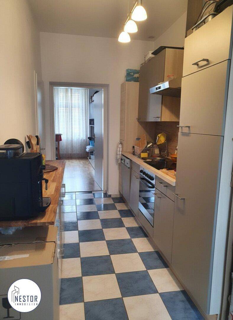 Schmale Küche mit kariertem Fliesenboden, Einbauküche und Blick in einen weiteren Raum.
