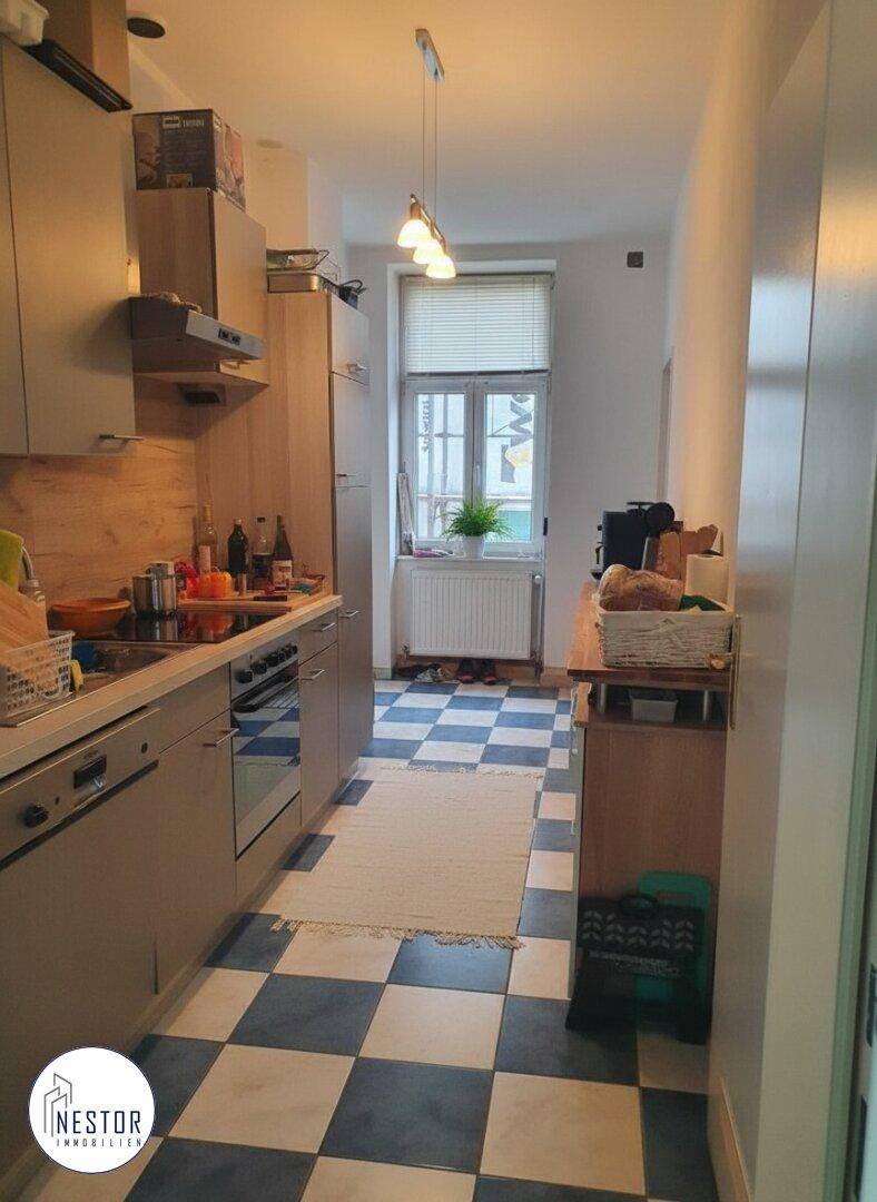 Funktionale Küche mit kariertem Boden, Holztheke und Fenster mit Jalousien.
