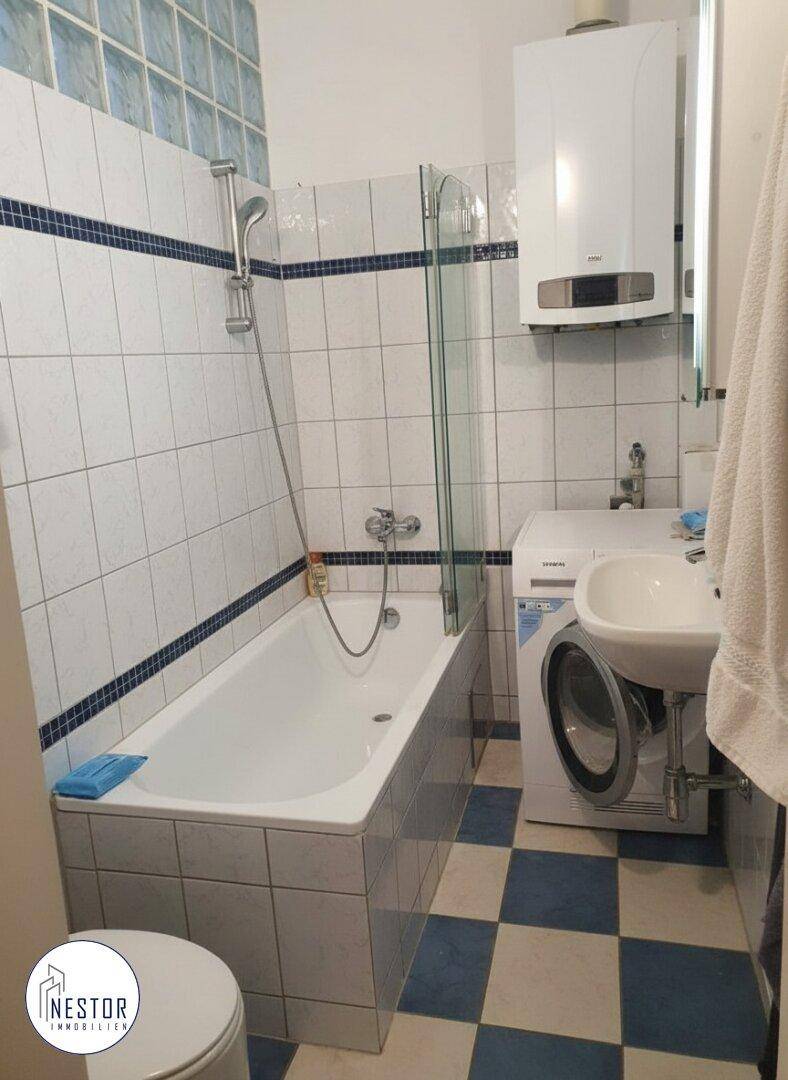 Badezimmer mit Badewanne, Waschbecken und Waschmaschine, gefliest in Weiß und Blau.
