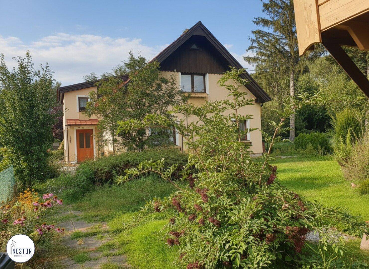 Seitenansicht des Hauses mit großem Rasenbereich, üppiger Bepflanzung und altem Baumbestand.