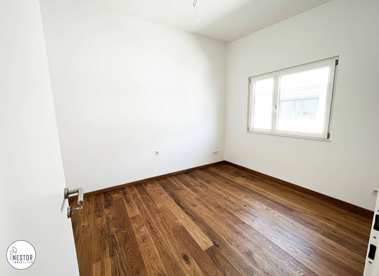 Leeres Zimmer mit Holzboden und einem Fenster, das für ausreichend Tageslicht sorgt.