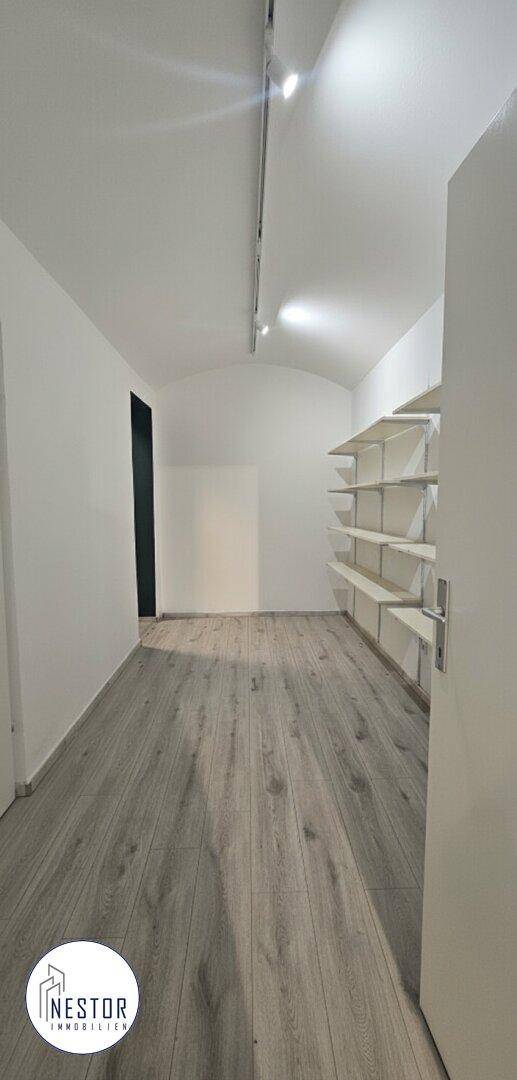 Heller Flur mit gewölbter Decke, Holzboden und praktischen weißen Regalen an der Wand.