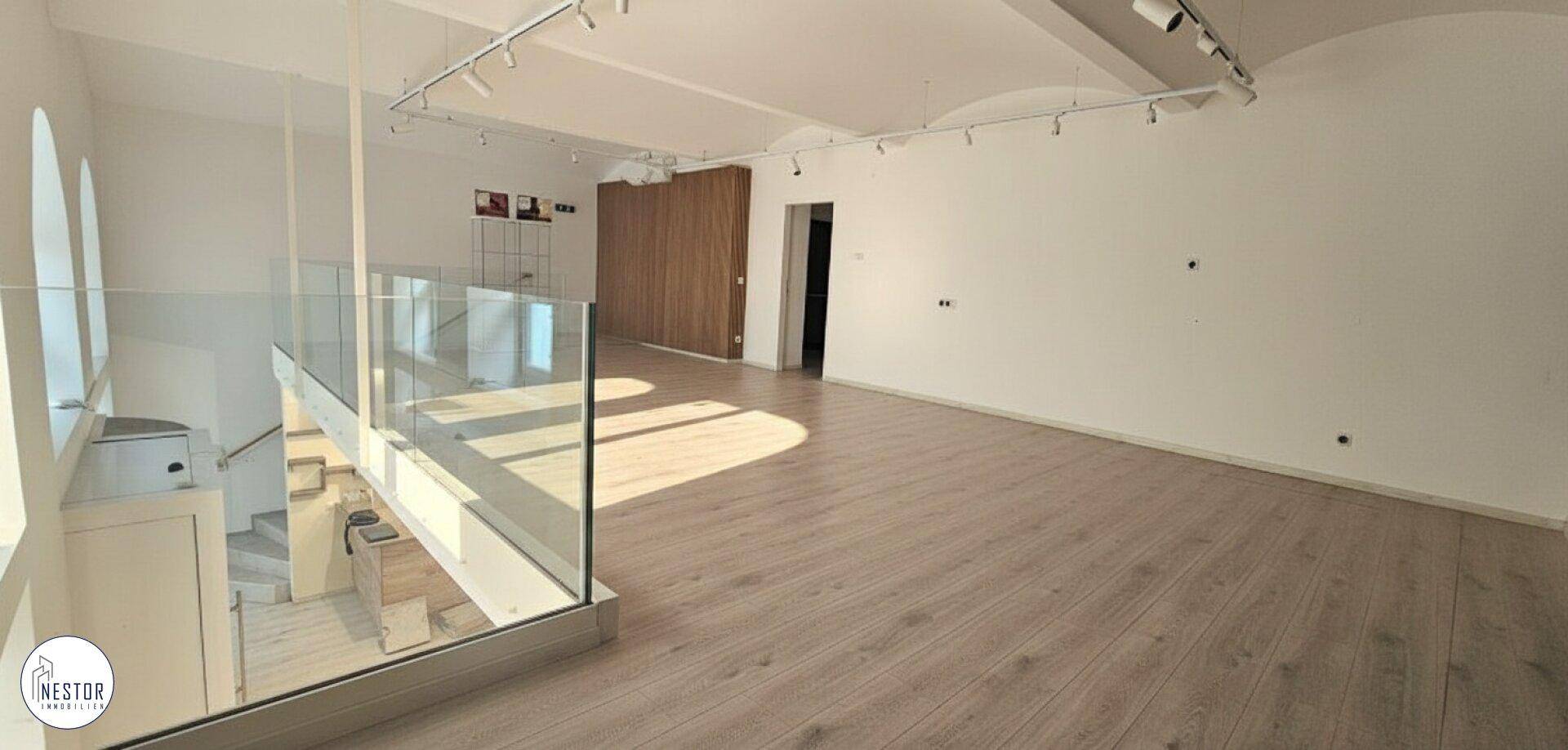 Heller, offener Raum mit gewölbter Decke, Holzboden und einer Treppe mit modernem Glasgeländer.