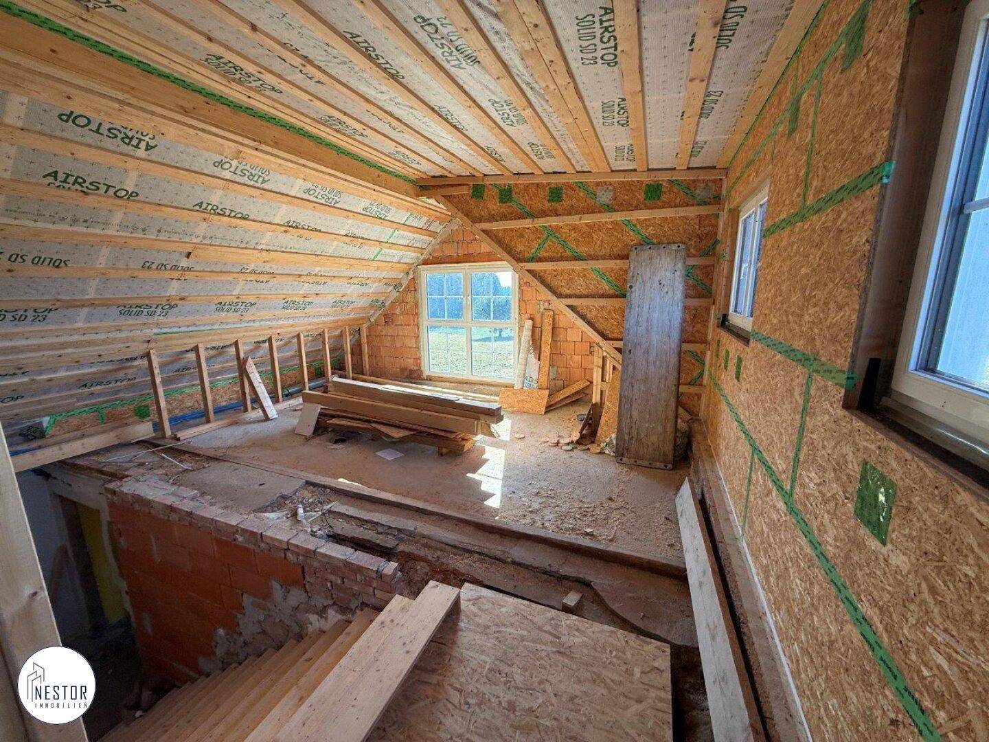 Dachgeschoss im Ausbau mit sichtbarer Holzkonstruktion und Fenstern, die viel Licht hereinlassen.