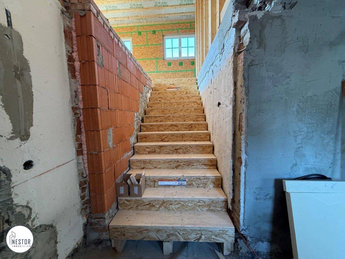 Treppenaufgang im Rohbau mit Holzstufen und unverputzten Ziegelwänden, bereit für den weiteren Ausbau.