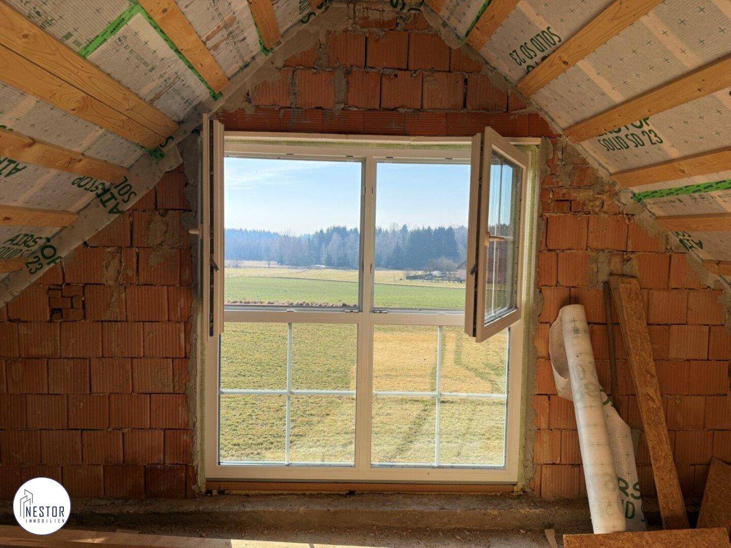 Großes Fenster im Dachgeschoss mit Blick auf die weite Landschaft und grüne Felder.