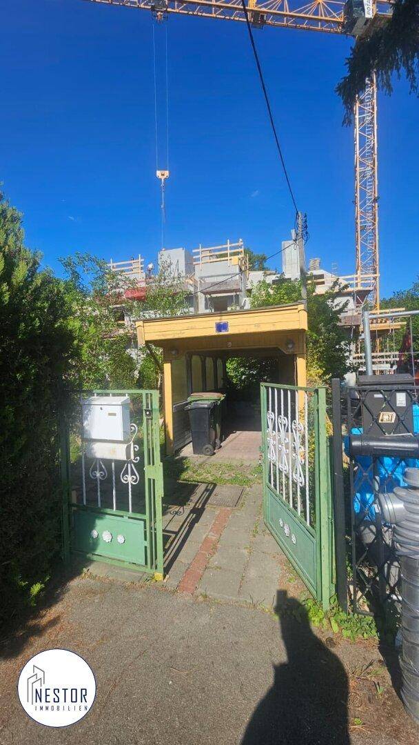 Eingangsbereich mit grünem Tor, Carport und einem Neubau mit Baugerüst im Hintergrund.
