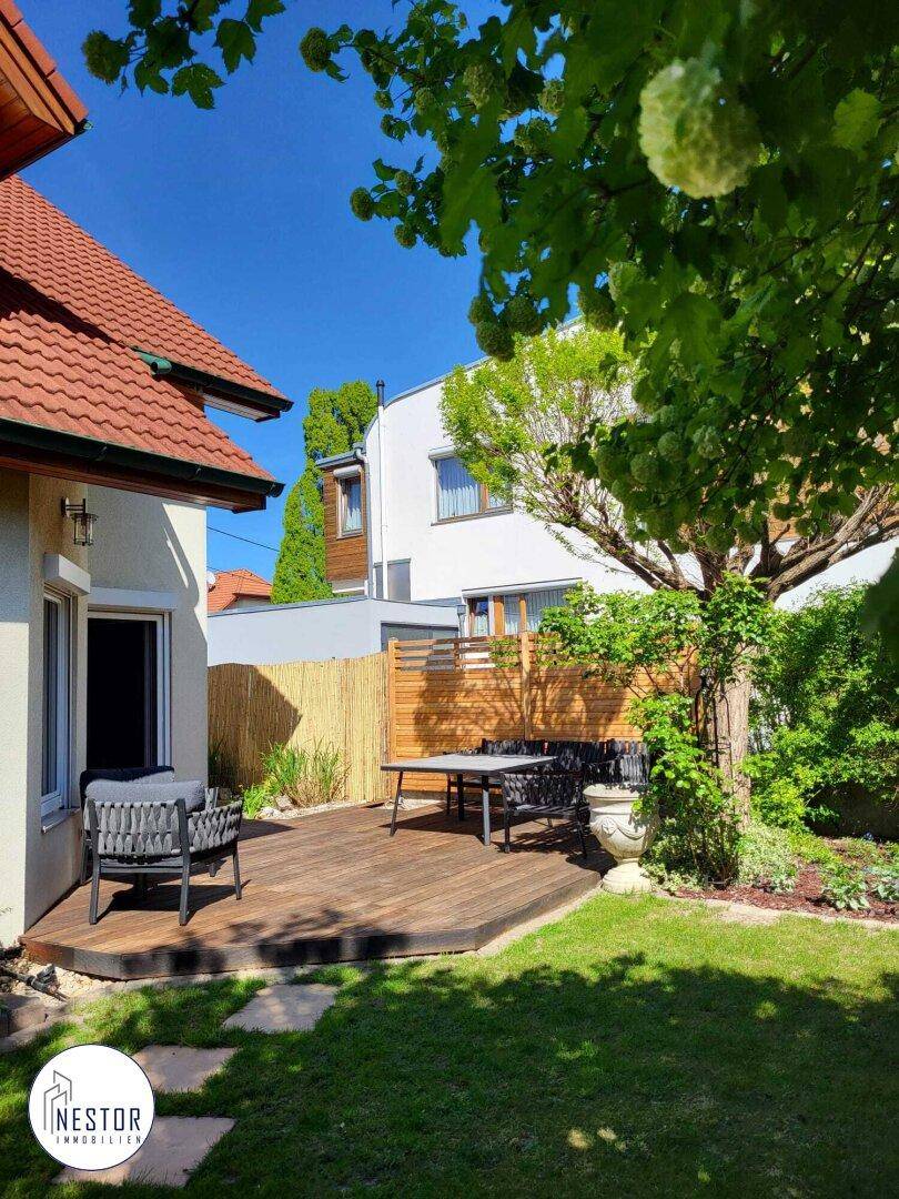 Weitläufige Holzterrasse mit Esstisch und Stühlen, umgeben von einem gepflegten Garten.