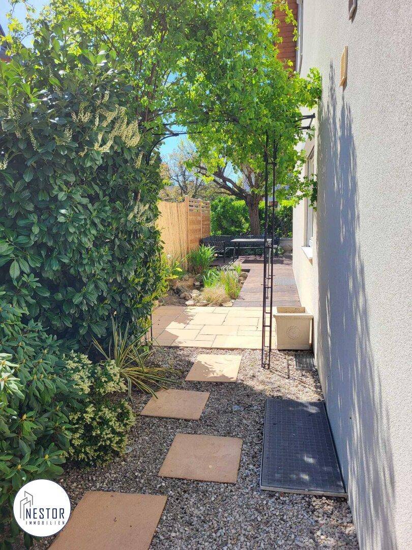 Schmaler Gartenweg mit Trittplatten, umgeben von üppigem Grün und Sträuchern.
