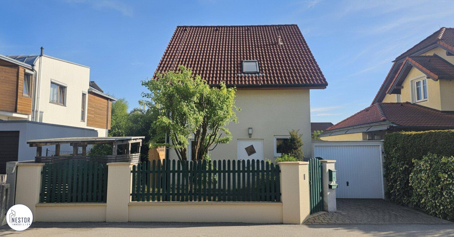 Vorderansicht des Hauses mit gepflegtem Vorgarten, Zaun und Garagenzufahrt.