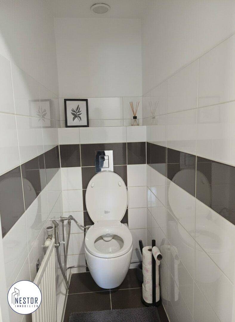Separate Toilette mit Wand-WC und dunklen Akzentfliesen.