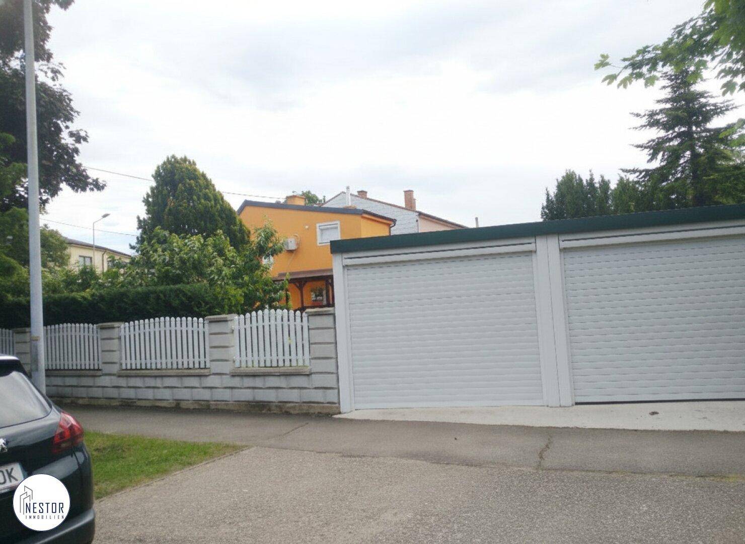 Doppelgarage mit Rolltoren und Zufahrt von der Straße, neben einem weißen Zaun.