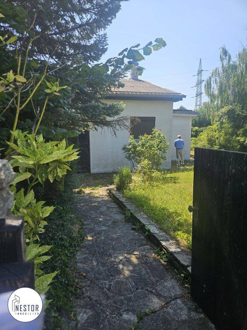 Kleines Gebäude im Garten mit einem Steinweg, umgeben von viel Grün an einem sonnigen Tag.