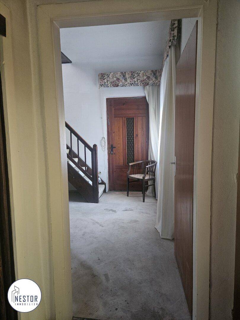 Flur mit Holztreppe und einer Holztür am Ende, die zu weiteren Räumen führt.