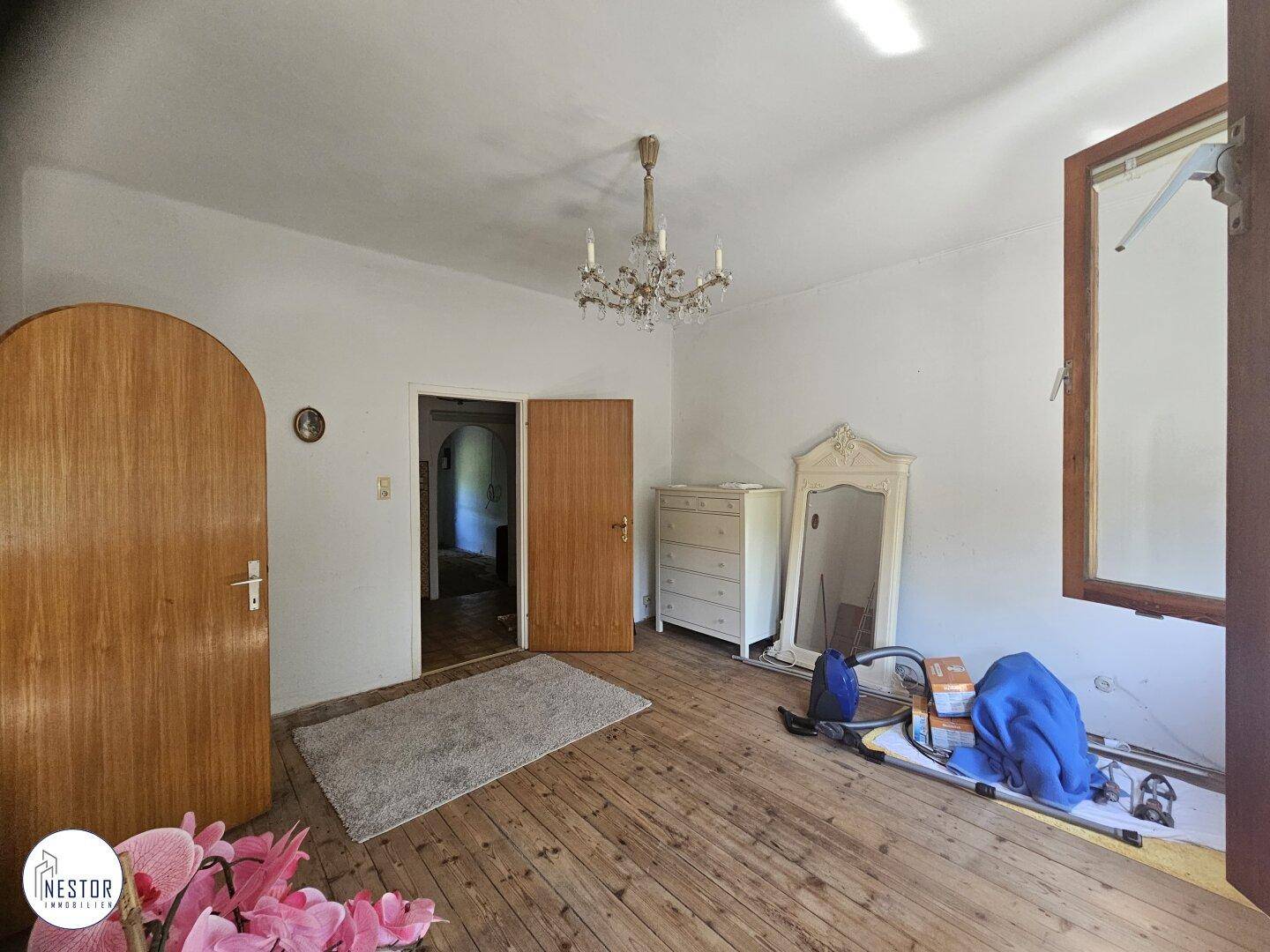 Geräumiges Schlafzimmer mit Holzdielenboden, Kronleuchter und einem großen Spiegel, mit Holztüren.