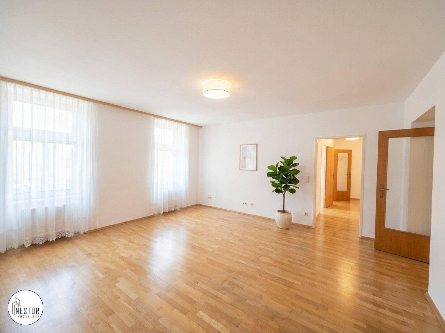 Helles und geräumiges Wohnzimmer mit Parkettboden, großen Fenstern und Zugang zu weiteren Räumen.