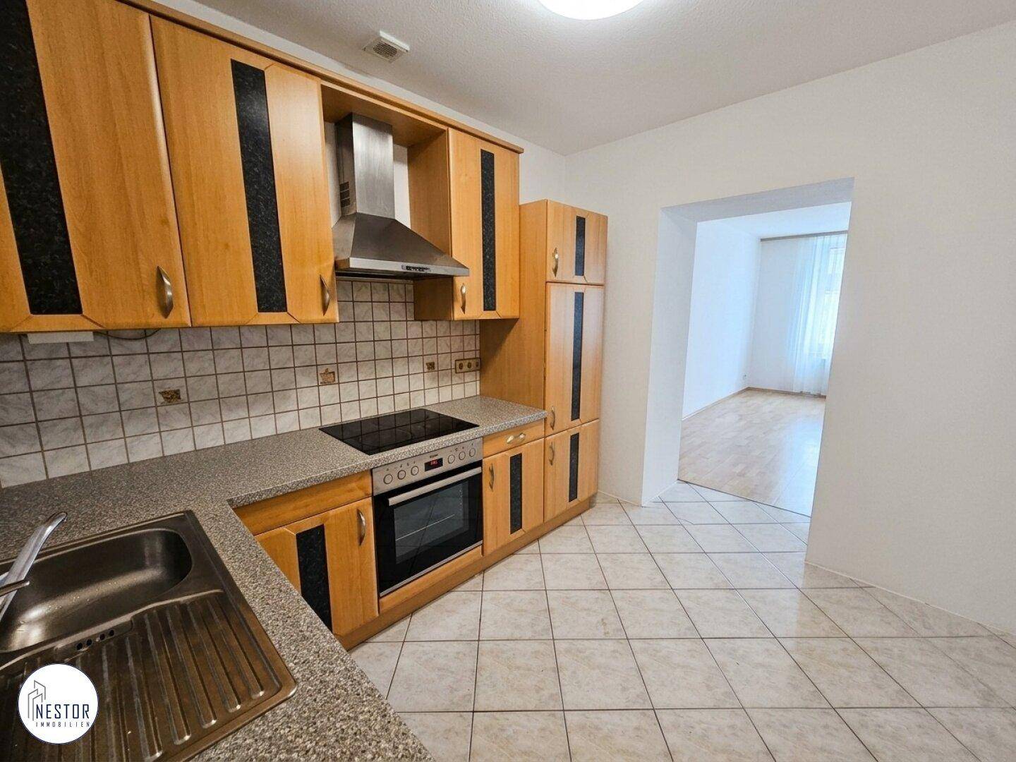 Funktionale Küche mit Holzschränken, Fliesenboden und integrierten Geräten, offen zu einem weiteren Raum.