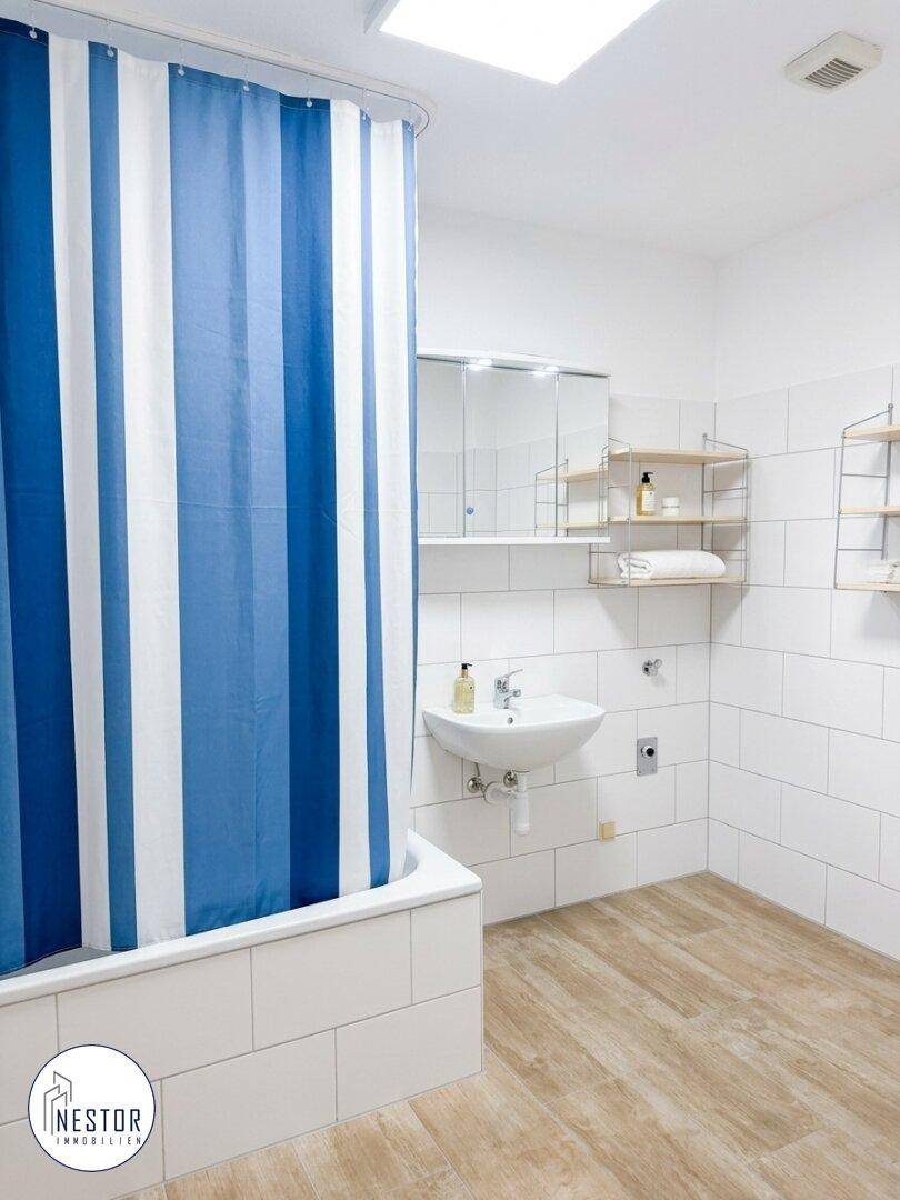 Helles Badezimmer mit Waschbecken, Spiegelschrank und Badewanne mit blau-weißem Duschvorhang.