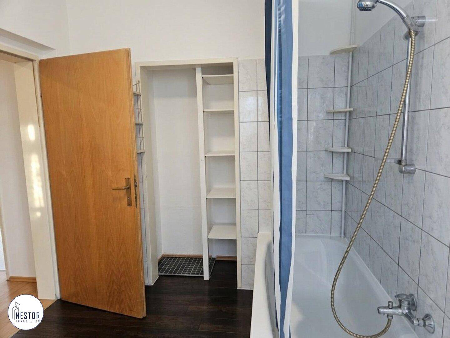 Badezimmer mit Badewanne und Duschvorhang, daneben ein praktischer Stauraum mit Regalen.