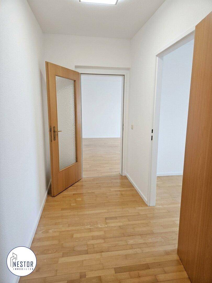 Heller Flur mit Parkettboden und Holztüren, der den Zugang zu verschiedenen Wohnbereichen ermöglicht.
