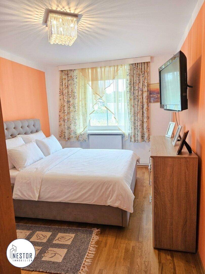 Gemütliches Schlafzimmer mit Doppelbett, floralen Vorhängen und einem an der Wand montierten Fernseher.