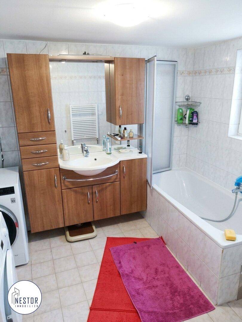 Geräumiges Badezimmer mit Badewanne, Waschbeckenunterschrank und Waschmaschine.