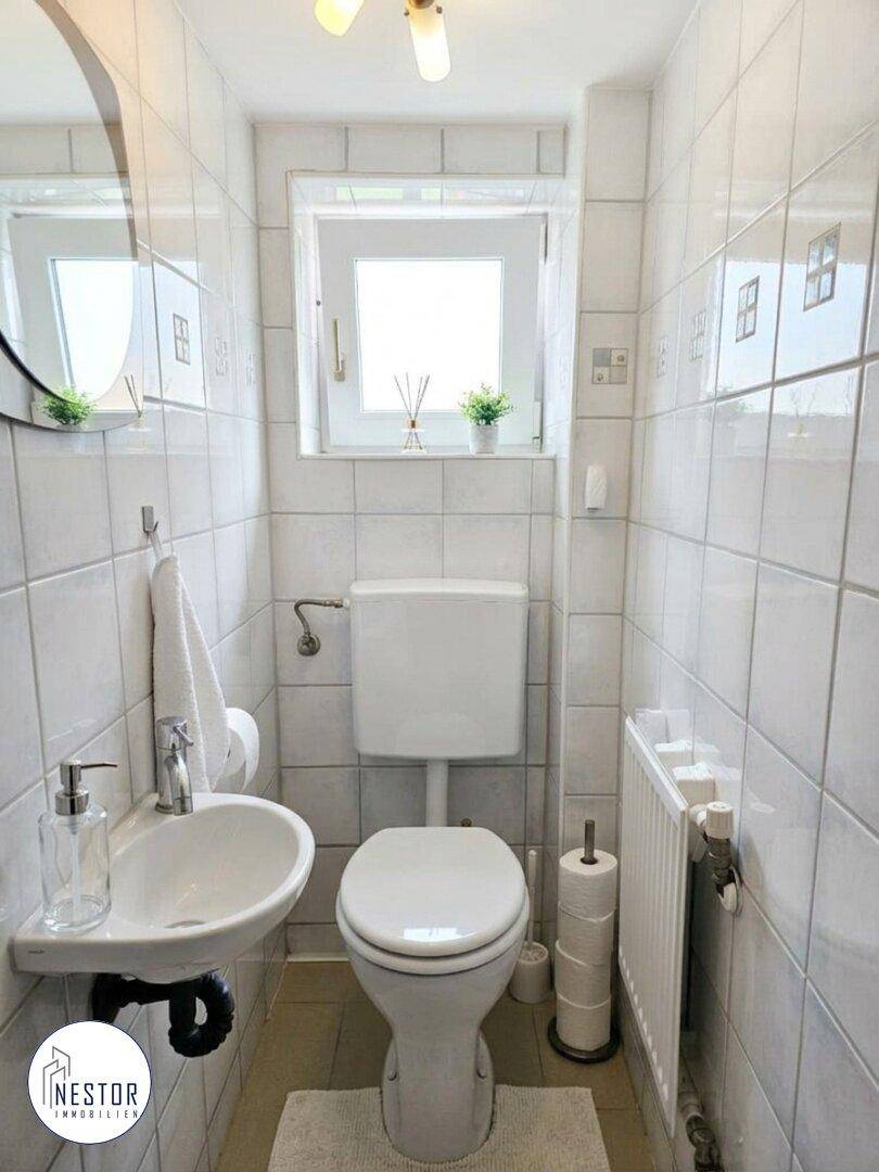 Kleines Gäste-WC mit Fenster, wandmontiertem WC und kleinem Waschbecken.