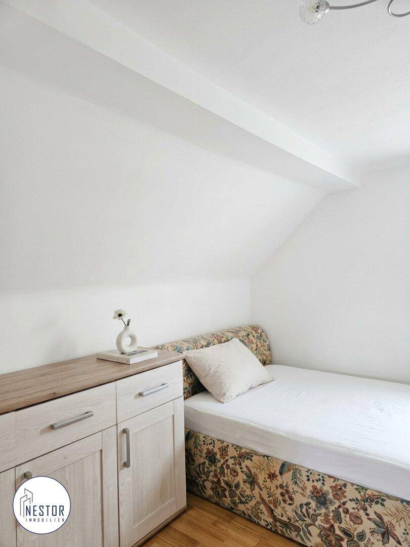 Helles Dachgeschosszimmer mit Einzelbett, Kommode und schrägen Wänden.