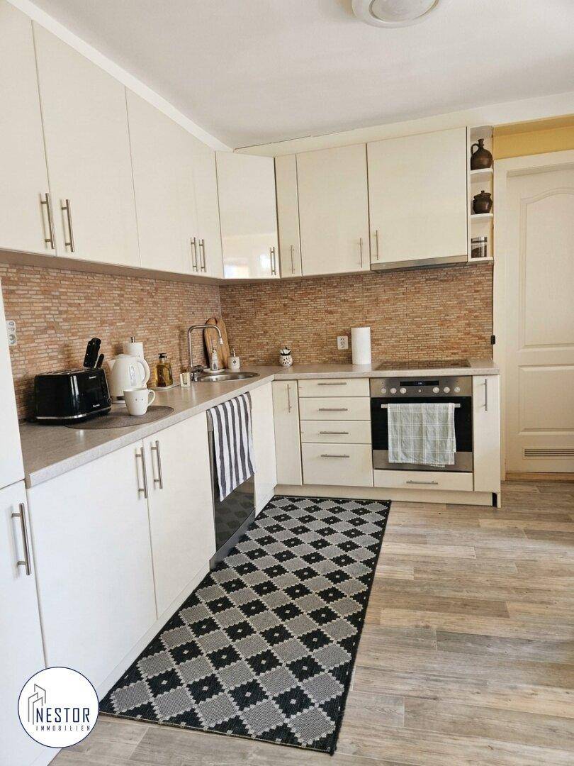 Moderne Küche mit weißen Schränken, Holzoptik-Boden und gemusterter Rückwand.