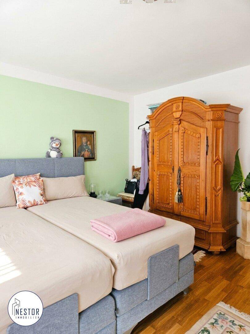 Schlafzimmer mit hellgrüner Akzentwand, Holzboden und einem großen, verzierten Holzschrank.